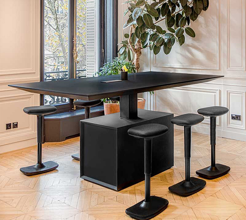 Schwarze Barhocker ohne Rückenlehne an einem hohen Tisch in einem modernen Büro mit großem Fenster